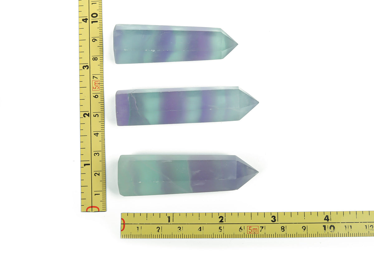 Polished fluorite obelisk tower crystal from GemstoneGO, showcasing vibrant green and purple hues in a tall, sleek shape.