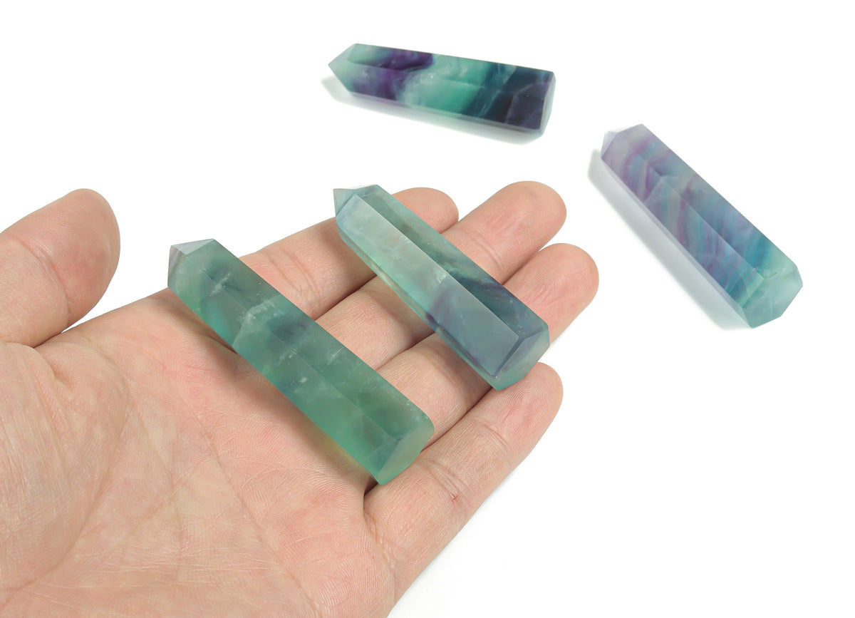 Polished fluorite obelisk tower crystal from GemstoneGO, showcasing vibrant green and purple mineral banding on a white background.