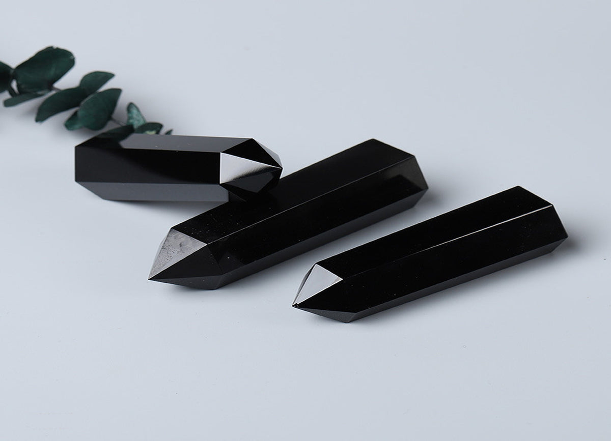 Dark obsidian obelisk tower crystal with smooth polished surface, showcasing natural stone patterns and sharp geometric shape.