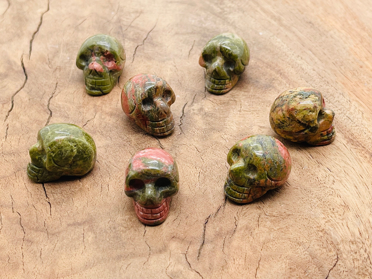 Unakite skull carved gemstone, 25mm, showing detailed green and pink mineral patterns on a polished surface.