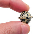 Mini Dalmatian Jasper Saturn crystal carved gemstone, 18mm planetary ornament, showcasing black spots on creamy stone surface.