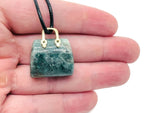 Moss agate crystal gemstone carved into a purse-shaped pendant, showcasing natural green and brown patterns with a silver bail attachment.