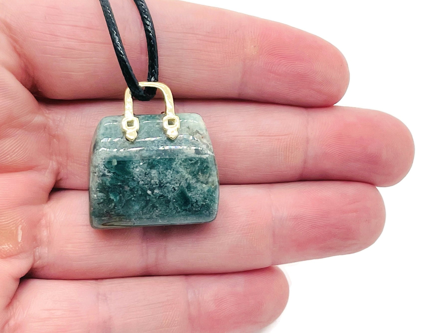 Moss agate crystal gemstone carved into a purse-shaped pendant, showcasing natural green and brown patterns with a silver bail attachment.