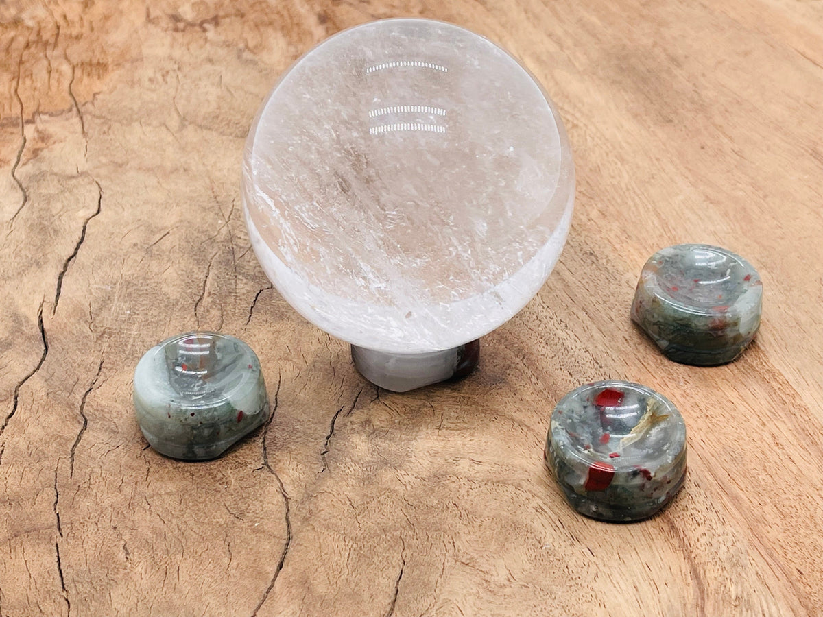 African Bloodstone crystal sphere on carved gemstone stand, used as elegant home decor piece, showcasing deep green and red hues.