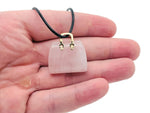 Rose quartz crystal carved into a handbag pendant, showcasing a smooth, pink gemstone with intricate detailing in the image.