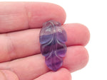 Fluorite leaf carving gemstone by GemstoneGO showing a vibrant green and purple carved leaf shape on a smooth surface.