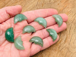 A 25mm Aventurine crystal moon face gemstone with carved smile design, showcasing a smooth, polished surface and natural green hue.