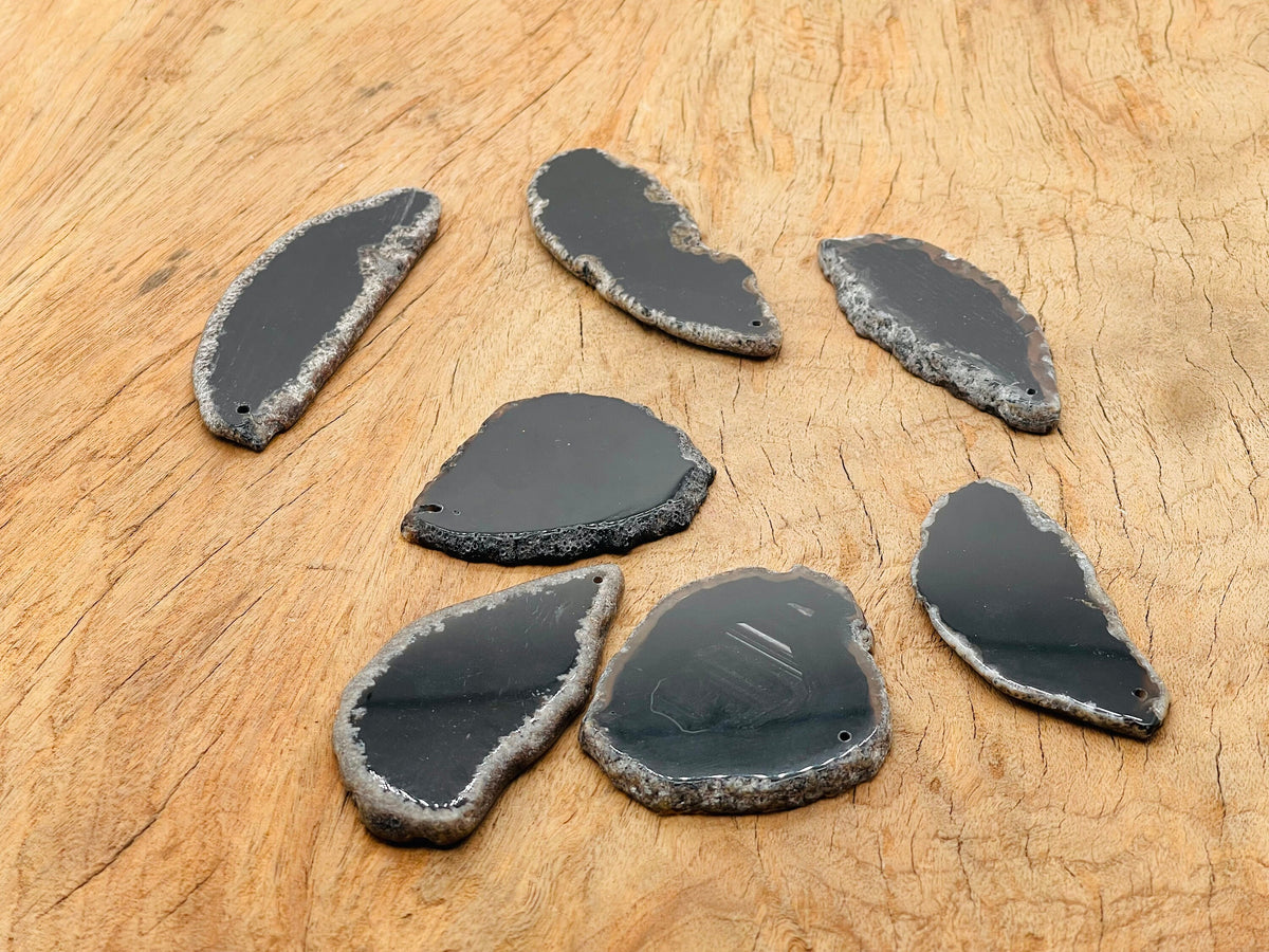 Black agate slice drilled pendant showing a smooth, polished black geode crystal with natural banding and a drilled hole for necklace use.