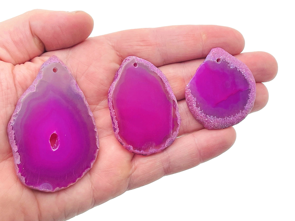 Pink agate slice drilled pendant with natural geode crystal details, showcasing a smooth, polished pink gemstone with a drilled hole for jewelry.
