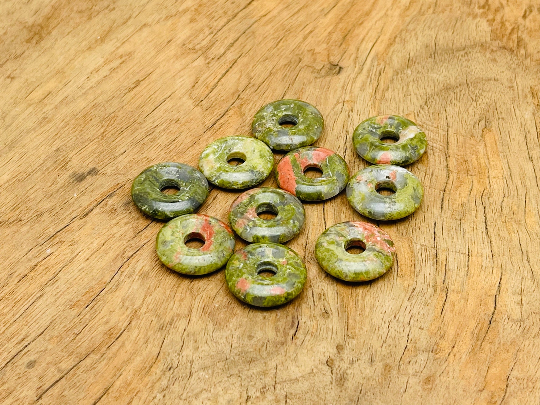 Unakite crystal donut pendant, 20mm Pi stone from GemstoneGO, showcasing pink and green mineral patterns on a white background.