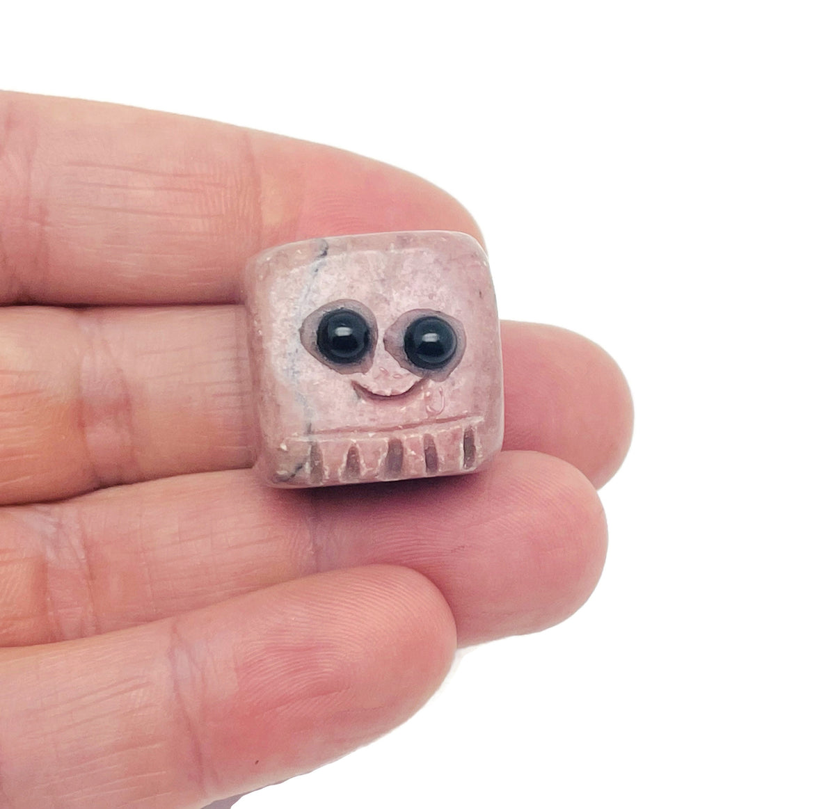 Rhodonite handmade carving skull gemstone from GemstoneGO, featuring a detailed pink and black stone sculpture on a plain background.