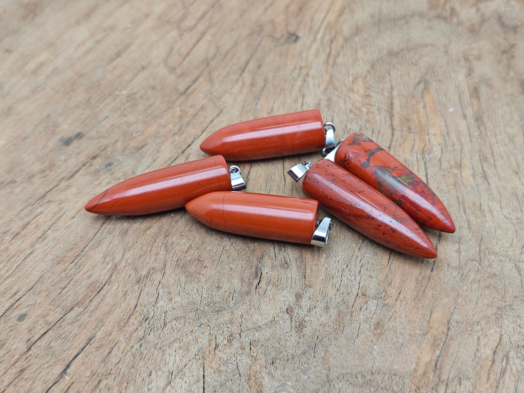 Polished red jasper bullet gemstone pendant with carved details, showcasing a smooth, natural red stone pendant on a plain background.