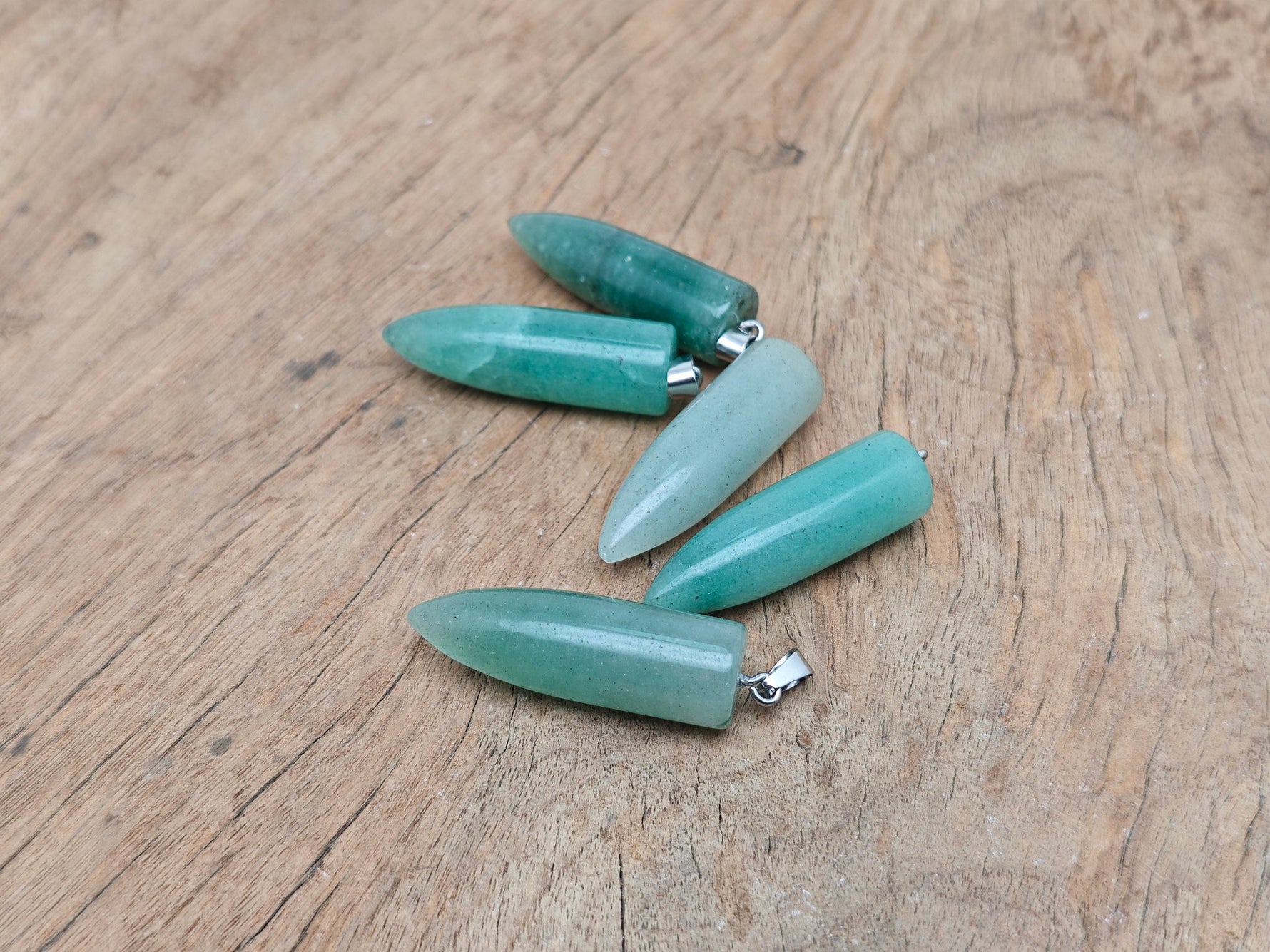 Polished aventurine bullet gemstone pendant with carved details, showcasing a smooth, natural green gemstone on a simple cord.
