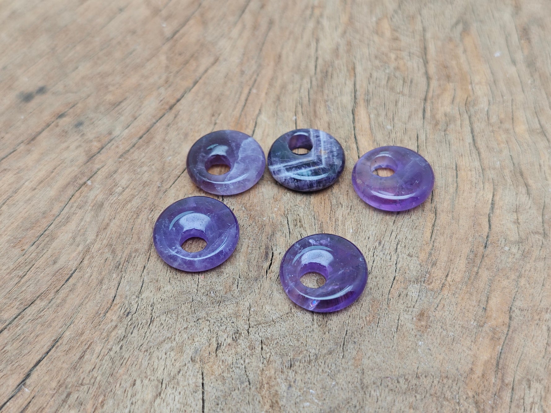 Amethyst crystal donut pendant from GemstoneGO, 18mm Pi stone with purple gemstone and smooth, polished surface.
