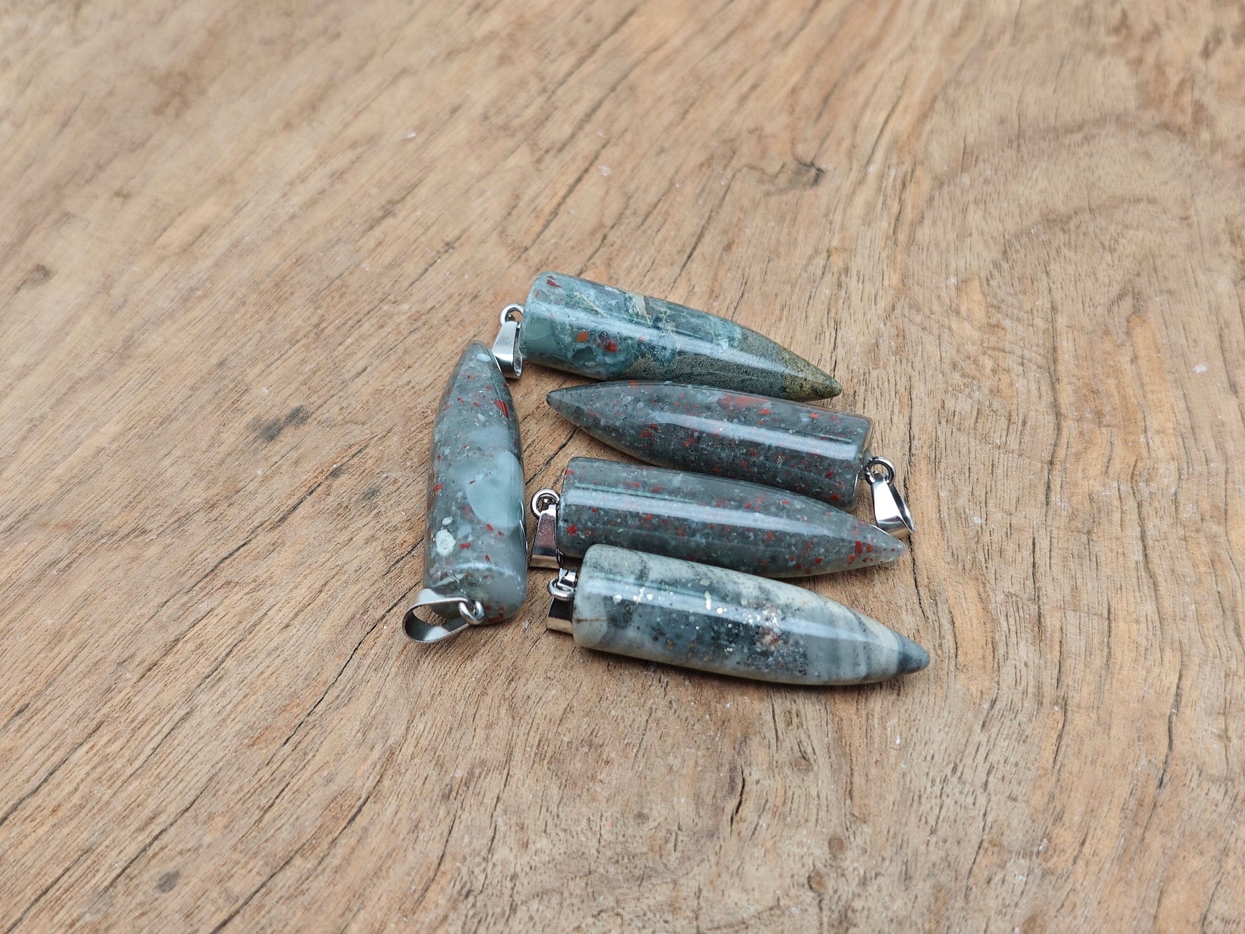 Polished African Bloodstone bullet-shaped gemstone pendant with carved details, showcasing deep green and red mineral patterns.
