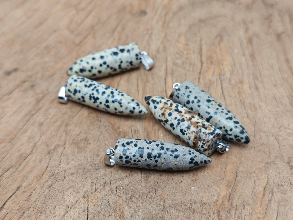 Polished Dalmatian Jasper bullet gemstone pendant with carved details, showcasing black spots on cream-colored stone.