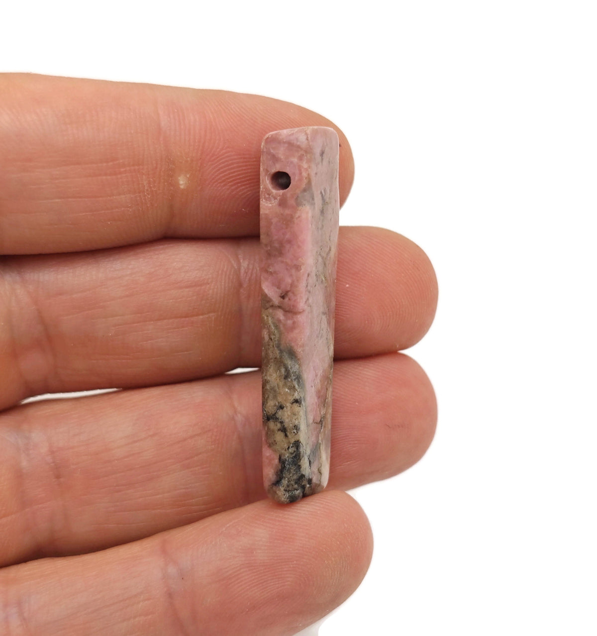 Rhodonite drilled tumbled gemstone pendant from GemstoneGO showcasing a smooth, pink and black stone with a drilled hole for jewelry.