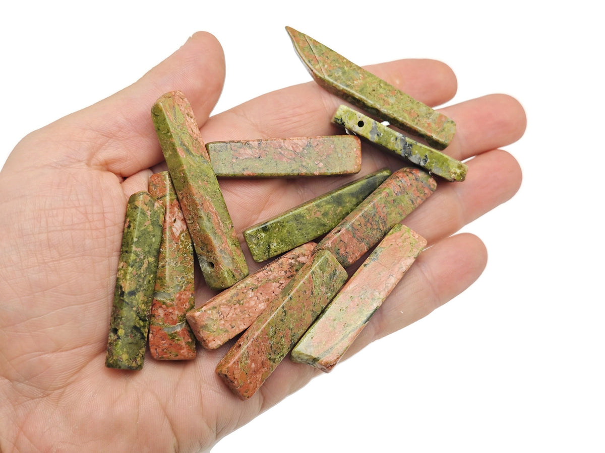 Unakite drilled tumbled gemstone pendant showing smooth, polished pink and green stone with a hole for jewelry attachment.