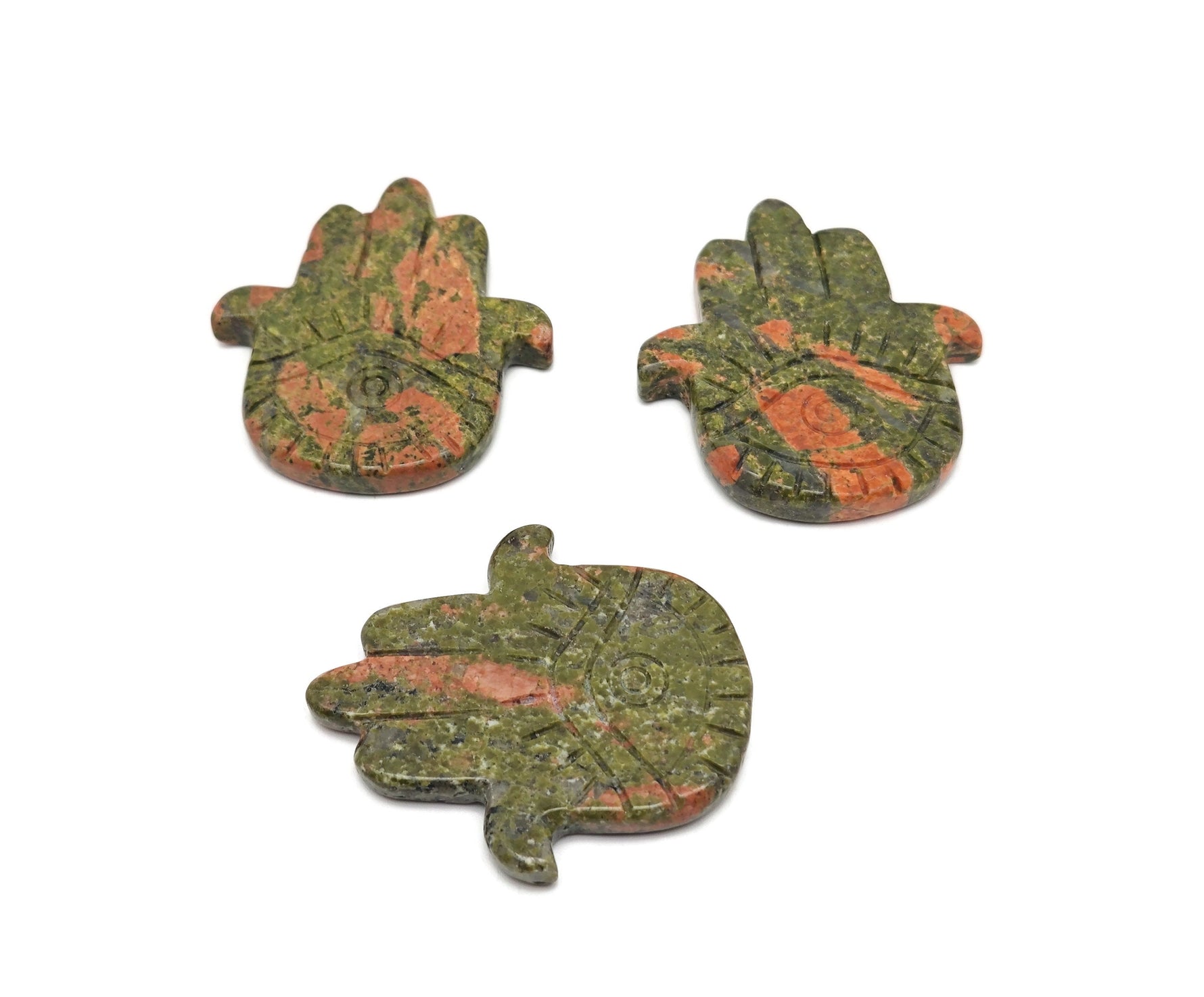 Unakite evil eye hand gemstone carving from GemstoneGO, detailed with vibrant green and pink hues, on a neutral background.