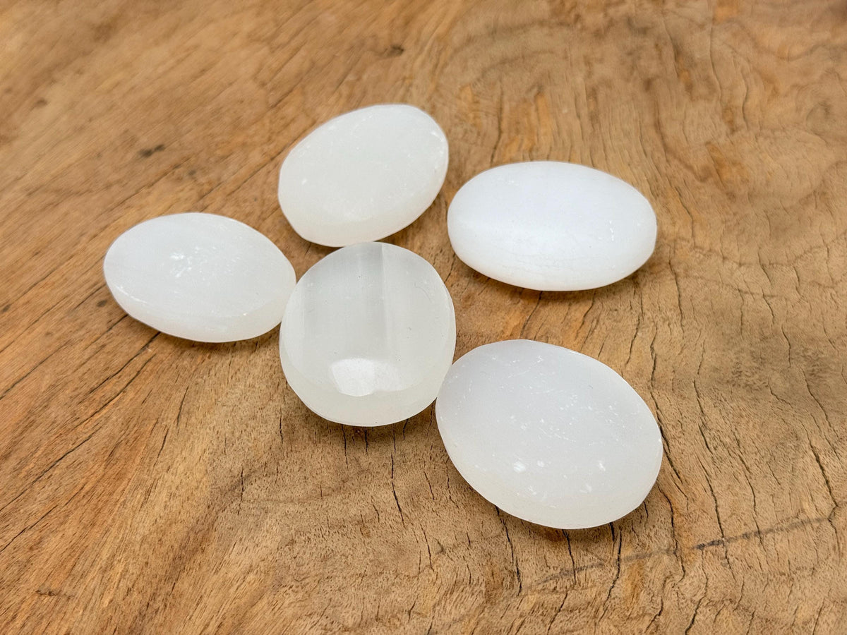 Selenite palm gemstone spa stone, 50mm size, smooth and polished, from GemstoneGO, resting on a neutral surface.