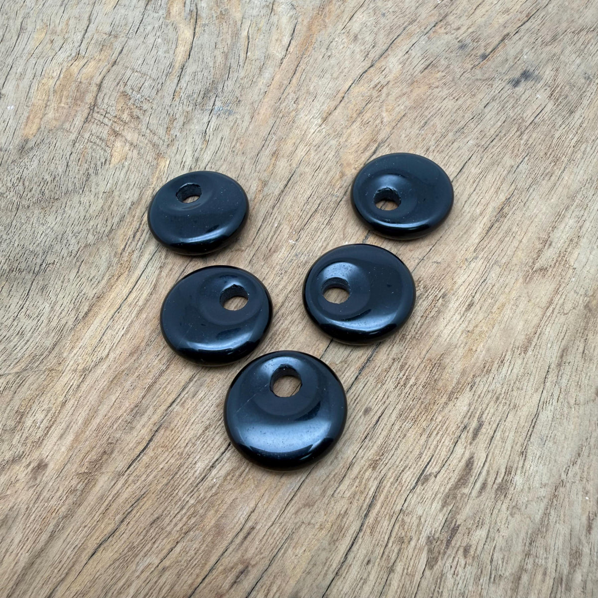 Polished 20mm obsidian crystal donut from GemstoneGO, showcasing a smooth, glossy black stone with natural patterns and a central hole.