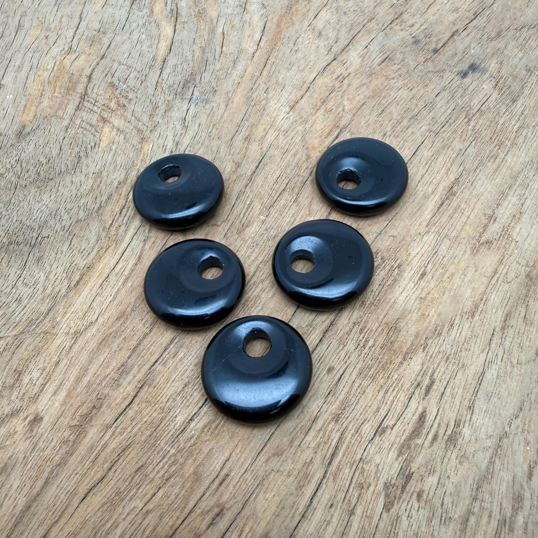 Polished 20mm obsidian crystal donut from GemstoneGO, showcasing a smooth, glossy black stone with natural patterns and a central hole.
