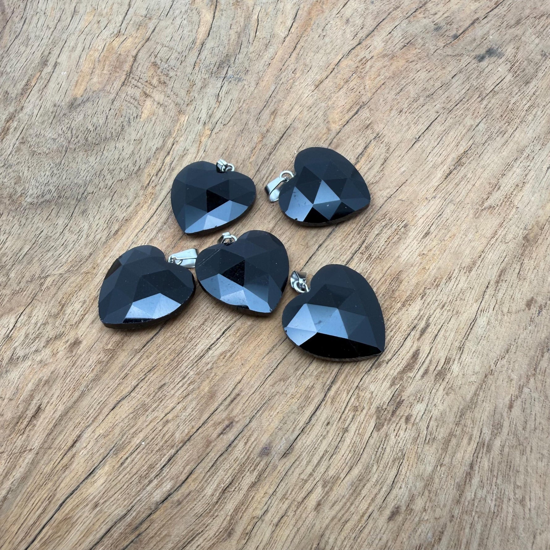 Faceted obsidian heart crystal pendant with natural gemstone charm, displayed on a silver chain. A striking gemstone jewelry piece.